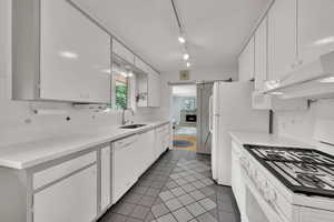 Kitchen with white appliances, white cabinetry, tile patterned flooring, and under cabinet range hood