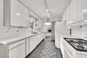 Kitchen with white appliances, white cabinets, tile patterned floors, under cabinet range hood, and decorative backsplash