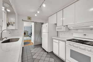 Kitchen featuring white appliances, white cabinetry, under cabinet range hood, and light tile patterned flooring