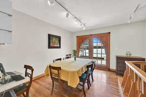 Dining room featuring rail lighting, light wood finished floors, a textured ceiling, and french doors