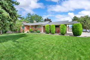 Ranch-style house with a front yard, a chimney, and brick siding