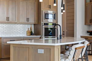 Kitchen with stainless steel appliances, decorative backsplash, a breakfast bar, a kitchen island with sink, and pendant lighting