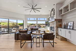 Living room with a ceiling fan, plenty of natural light, a stone fireplace, light wood finished floors, and recessed lighting