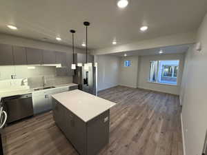 Kitchen featuring stainless steel appliances, a center island, recessed lighting, wood finished floors, and light countertops