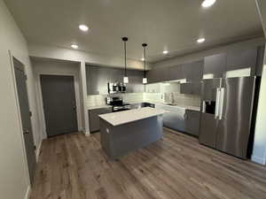 Kitchen featuring appliances with stainless steel finishes, gray cabinetry, wood finished floors, recessed lighting, and a center island