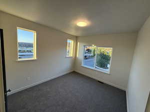 Spare room featuring healthy amount of natural light, a textured ceiling, and dark carpet