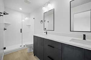 Full bath featuring wood finished floors, double vanity, a stall shower, and recessed lighting
