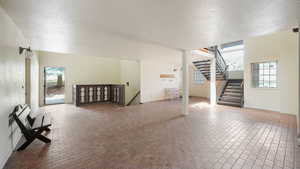 Unfurnished living room with brick patterned flooring, healthy amount of natural light, a textured ceiling, and stairway