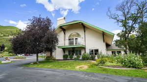 View of side of home with stucco siding, a chimney, and a yard