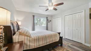 Bedroom with two closets, wood finished floors, a textured ceiling, and ceiling fan