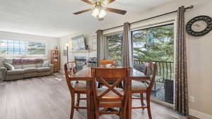 Dining room featuring ceiling fan, wood finished floors, a tiled fireplace, and a textured ceiling