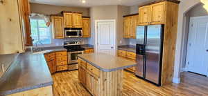 Kitchen featuring appliances with stainless steel finishes, light wood-style flooring, arched walkways, a center island, and dark countertops