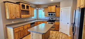 Kitchen with stainless steel appliances, light wood-style flooring, recessed lighting, a center island, and glass insert cabinets