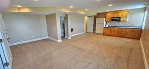 Kitchen with light carpet, freestanding refrigerator, recessed lighting, stainless steel microwave, and brown cabinetry