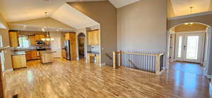 Kitchen with arched walkways, a chandelier, a center island, light wood-style floors, and high vaulted ceiling