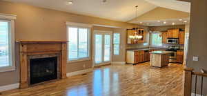 Kitchen featuring a kitchen island, stainless steel appliances, light wood-style flooring, lofted ceiling, and a tiled fireplace