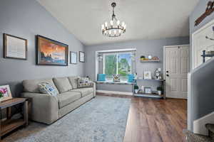 Living area with a chandelier, wood finished floors, and vaulted ceiling