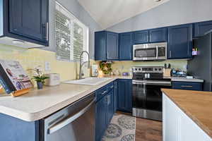 Kitchen featuring blue cabinetry, stainless steel appliances, light countertops, lofted ceiling, and dark wood finished floors