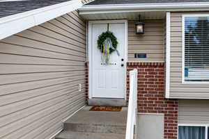 Entrance to property with a shingled roof and brick siding