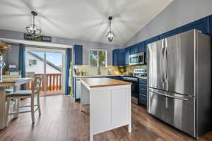 Kitchen with blue cabinets, appliances with stainless steel finishes, wooden counters, tasteful backsplash, and vaulted ceiling