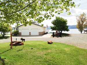 View of grassy yard featuring a water view, driveway, and a garage