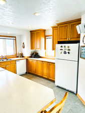 Kitchen with white appliances, brown cabinetry, light countertops, a textured ceiling, and recessed lighting