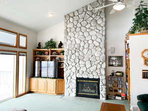 Living area featuring vaulted ceiling, a ceiling fan, a fireplace, and carpet flooring