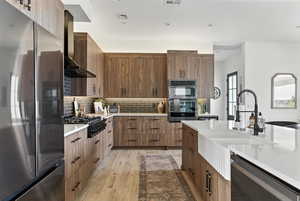Kitchen with light countertops, wall chimney exhaust hood, light wood-type flooring, and backsplash