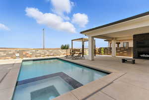 View of pool with a patio, a pool with connected hot tub, exterior fireplace, and a fenced backyard