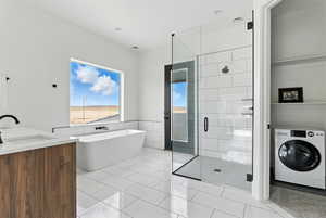 Bathroom featuring washer / dryer, a shower stall, a soaking tub, tile walls, and vanity