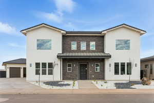 View of front facade featuring stone siding, stucco siding, driveway, a garage, and a standing seam roof
