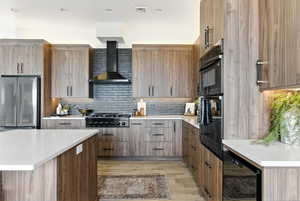 Kitchen featuring appliances with beautiful finishes, light countertops, light wood-type flooring, wall chimney range hood, and recessed lighting