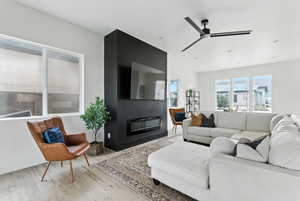 Living area featuring wood finished floors, a glass covered fireplace, and a ceiling fan