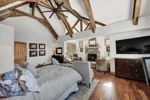 Bedroom featuring a lit fireplace, dark wood-style floors, beam ceiling, and high vaulted ceiling