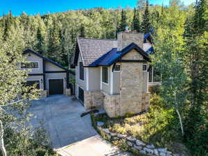 View of front facade featuring stone siding, driveway, a forest view, and a chimney