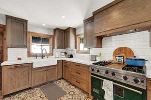 Kitchen with designer stove, decorative backsplash, wall chimney exhaust hood, light countertops, and recessed lighting