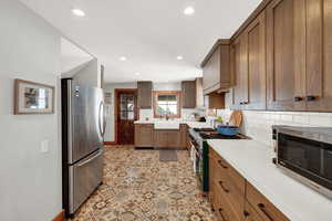 Kitchen featuring stainless steel appliances, decorative backsplash, light countertops, recessed lighting, and brown cabinetry