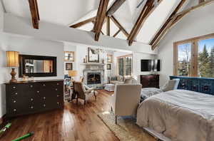 Bedroom with high vaulted ceiling, dark wood-style flooring, beam ceiling, multiple windows, and a stone fireplace