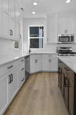 Kitchen featuring light wood-style flooring, decorative backsplash, stainless steel appliances, white cabinets, and recessed lighting