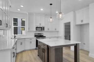 Kitchen with appliances with stainless steel finishes, tasteful backsplash, white cabinets, light stone counters, and light wood finished floors