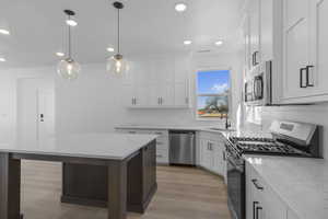 Kitchen with stainless steel appliances, backsplash, a center island, light wood-style floors, and recessed lighting