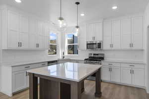 Kitchen with stainless steel appliances, white cabinets, light wood finished floors, backsplash, and decorative light fixtures