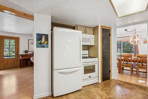 Kitchen with white appliances, light wood-style flooring, a chandelier, and healthy amount of natural light