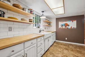 Kitchen with open shelves, wooden counters, tasteful backsplash, white cabinetry, and white dishwasher