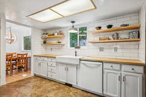 Kitchen featuring butcher block counters, open shelves, white dishwasher, and healthy amount of natural light