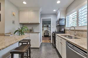 Kitchen with appliances with stainless steel finishes, white cabinets, a kitchen breakfast bar, light stone counters, and recessed lighting