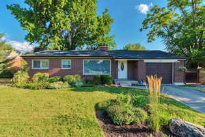 Single story home featuring brick siding, an attached garage, a front yard, and a chimney