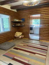 Hall featuring washing machine and dryer, wood finished floors, beam ceiling, and log walls