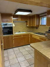 Kitchen featuring oven, light countertops, light tile patterned floors, electric stovetop, and brown cabinetry