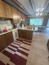 Kitchen featuring white gas range oven, light countertops, a peninsula, brown cabinetry, and decorative backsplash